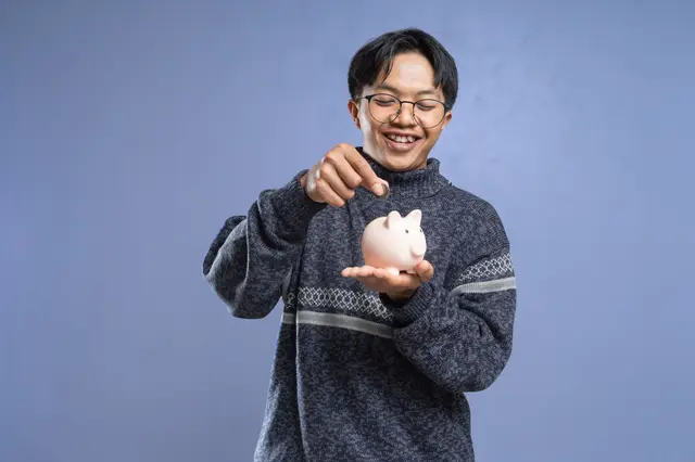A young man smiling as he saves into a piggy bank