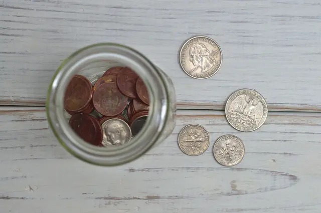 A glass jar of saved coins on a wooden table